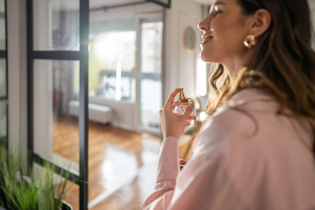 Smiling woman applying perfume in hallway while