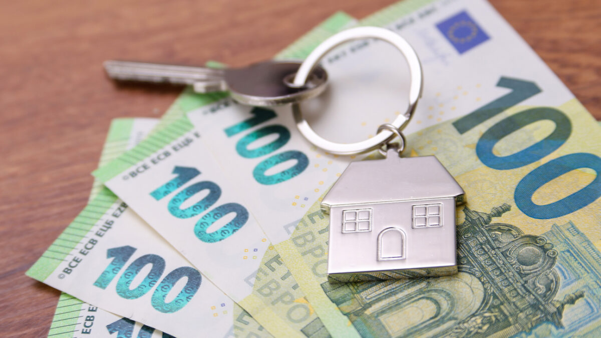 House key symbol pendant on one hundred euro banknotes, fanned out on a wooden desk