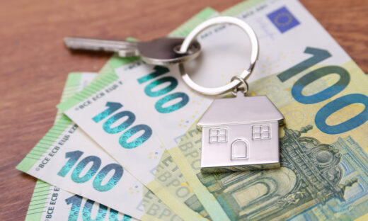 House key symbol pendant on one hundred euro banknotes, fanned out on a wooden desk