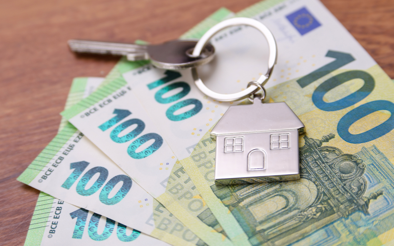 House key symbol pendant on one hundred euro banknotes, fanned out on a wooden desk