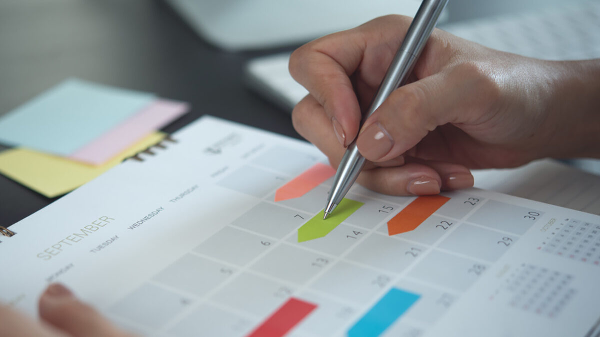 Closeup, woman hand writing on calendar event planner to set timetable organize schedule, event planning for business meeting or vacation plan. Organization and business planning concept.