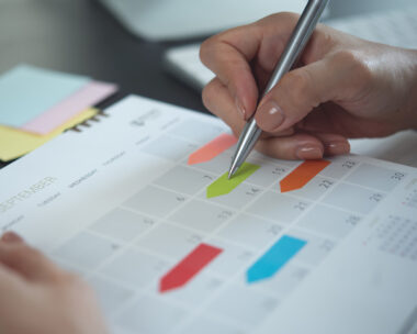 Closeup, woman hand writing on calendar event planner to set timetable organize schedule, event planning for business meeting or vacation plan. Organization and business planning concept.