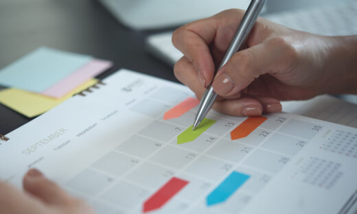 Closeup, woman hand writing on calendar event planner to set timetable organize schedule, event planning for business meeting or vacation plan. Organization and business planning concept.