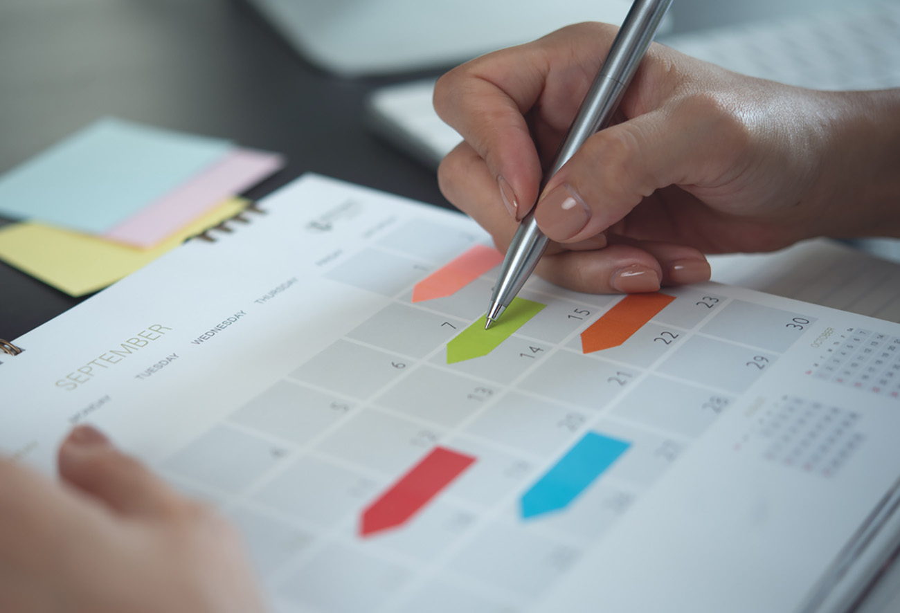Closeup, woman hand writing on calendar event planner to set timetable organize schedule, event planning for business meeting or vacation plan. Organization and business planning concept.
