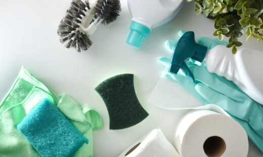 Bathroom cleaning supplies such as disinfectant bottles, scouring pads, gloves, toilet brush and toilet paper on white wooden table. Top view.