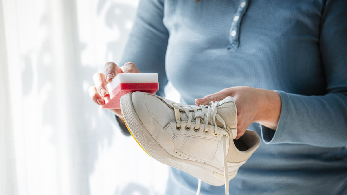 Unrecognizable woman rubbing white sneakers with a special cleaning sponge at home