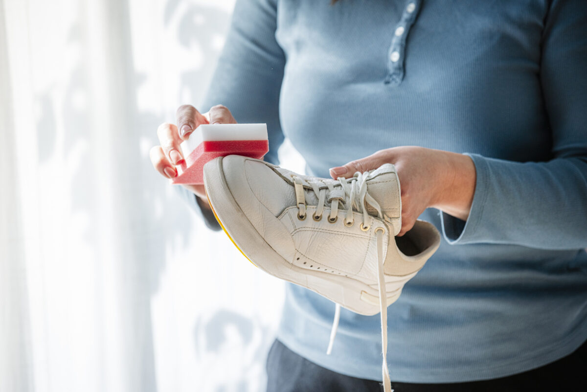 Unrecognizable woman rubbing white sneakers with a special cleaning sponge at home