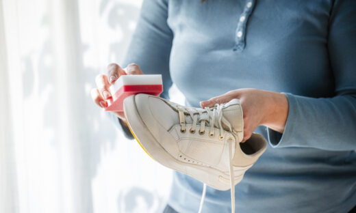 Unrecognizable woman rubbing white sneakers with a special cleaning sponge at home