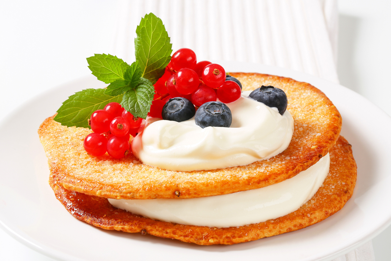 detail of pancakes with berry fruits and whipped cream on white plate