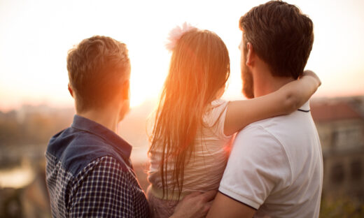Young gay parents with their daughter having fun in park. Parents holding girl in arms. Enjoying in beautiful sunset. Caucasian ethnicity
