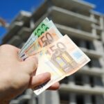 Man holding euro money in front of block building in build process
