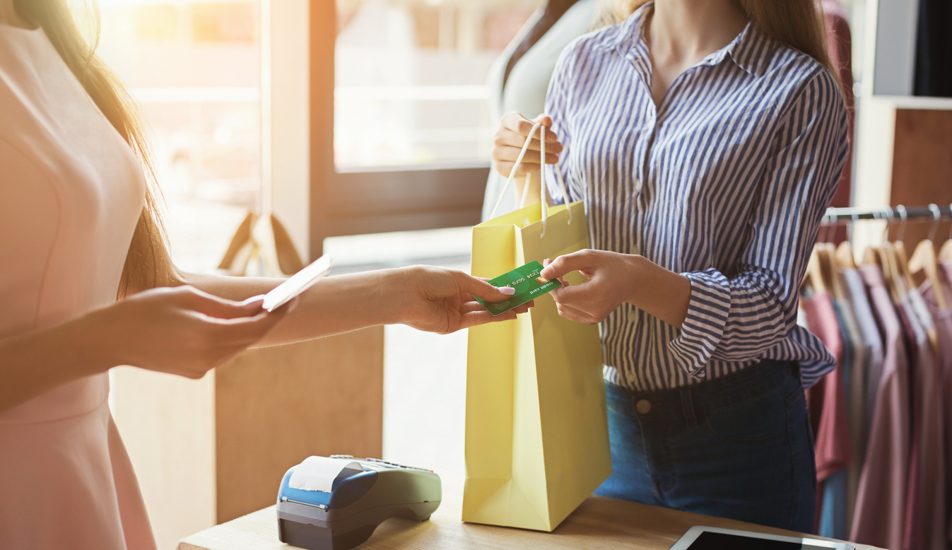 Woman paying with credit card for purchase at clothes showroom. Finance and non-cash transaction concept
