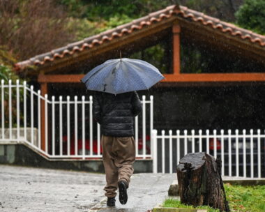 Ένας άνδρας περπατάει στη βροχή κρατώντας μία ομπρέλα