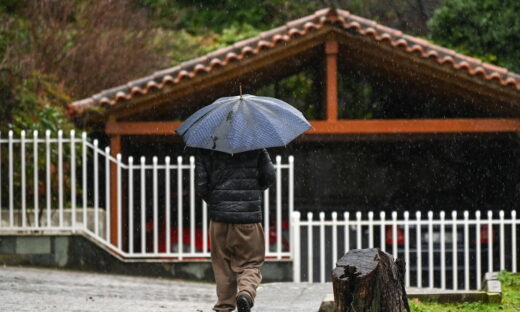 Ένας άνδρας περπατάει στη βροχή κρατώντας μία ομπρέλα