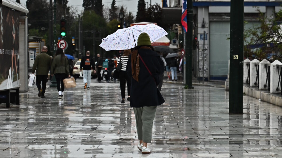Μία γυναίκα περπατάει στη βροχή κρατώντας ομπρέλα