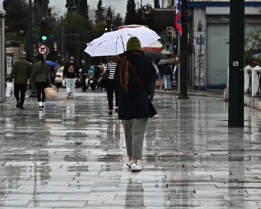 Μία γυναίκα περπατάει στη βροχή κρατώντας ομπρέλα