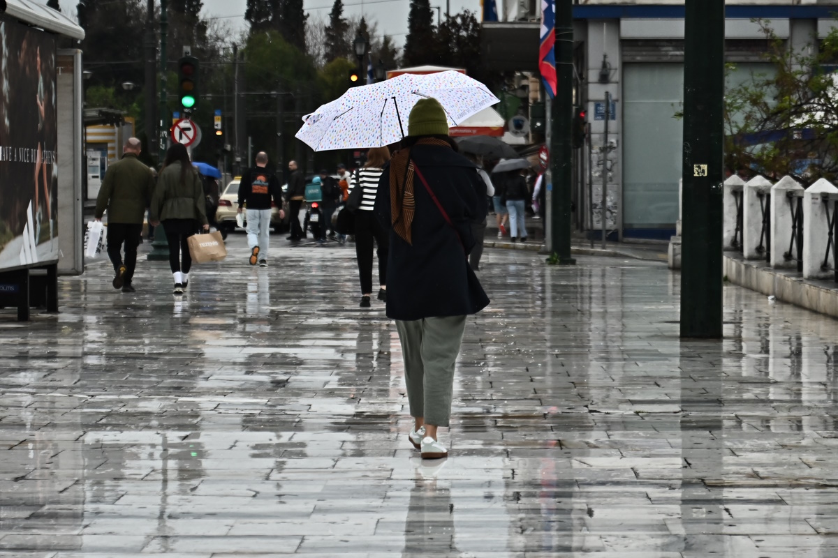 Μία γυναίκα περπατάει στη βροχή κρατώντας ομπρέλα