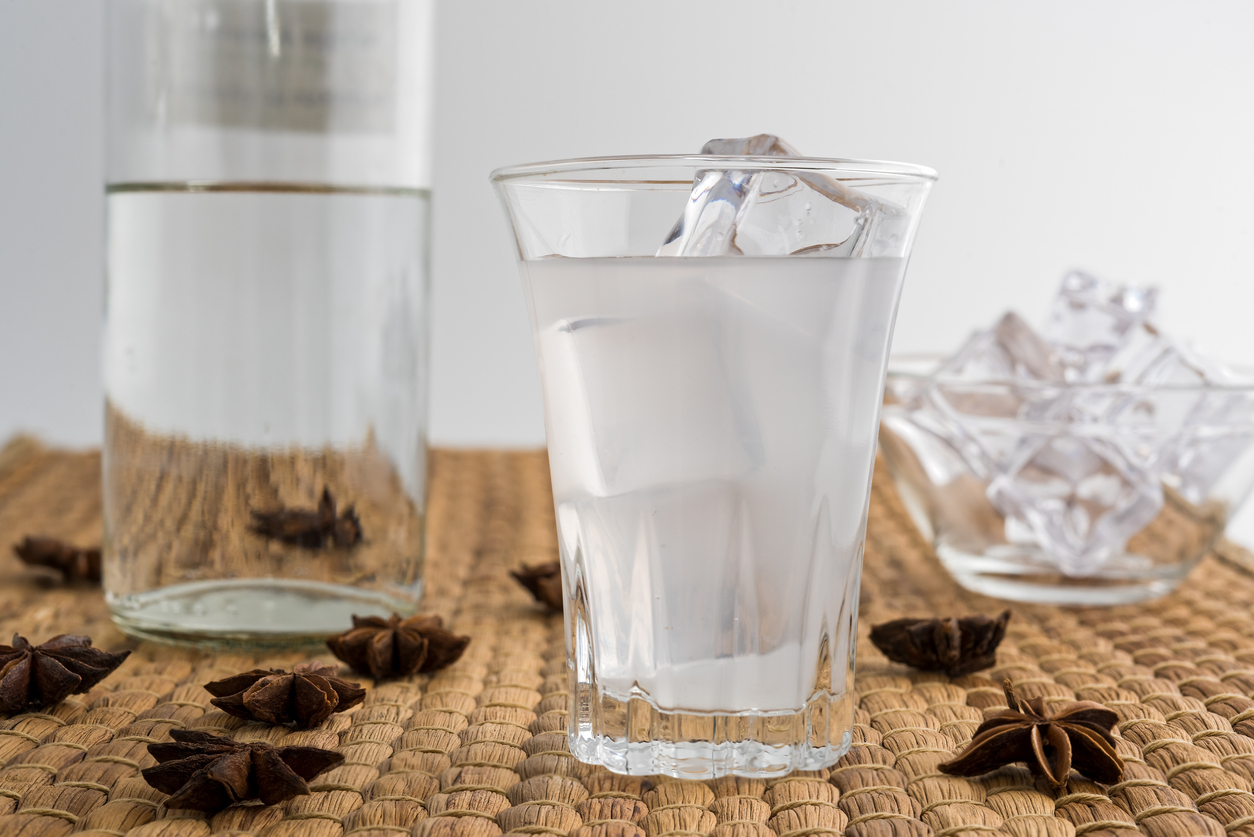 Glass and bottle of traditional drink Ouzo or Raki with anise star seeds on natural matting