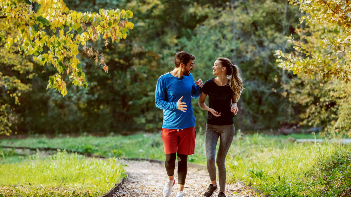 Full length of cute caucasian couple in sportswear walking on trail in woods, smiling and talking