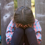 Crying caucasian child girl sitting on the floor covering his face