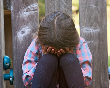 Crying caucasian child girl sitting on the floor covering his face