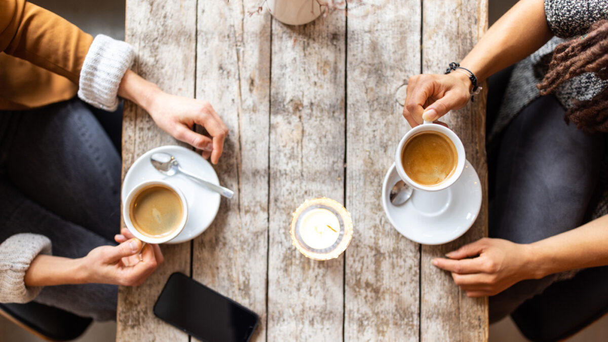 Top view cropped shot of two women sitting at cafe with coffee cups and mobile phone over table. Female friends meeting a coffee shop.