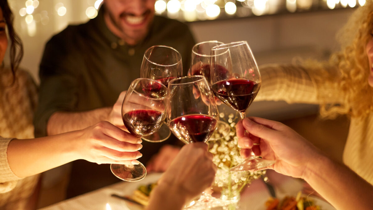 holidays, celebration and people concept - happy friends having christmas dinner at home drinking non-alcoholic red wine