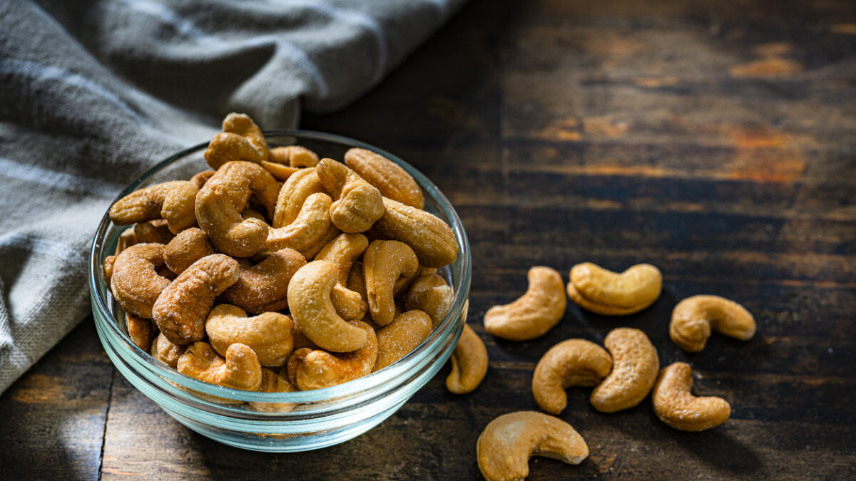 Close up view of a glass bowl filled with peanuts shot on dark rustic table.