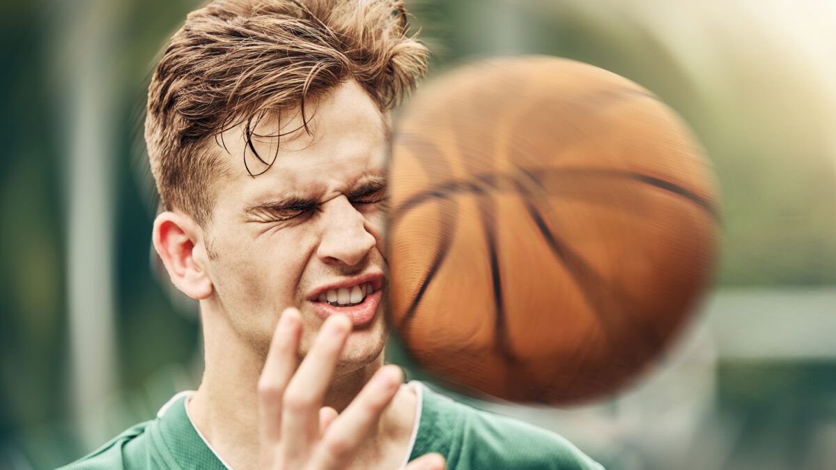 Sports, basketball and accident with face in game match on athlete court for tournament training. Injured man in professional outdoor fitness centre in pain from impact of ball hit action.