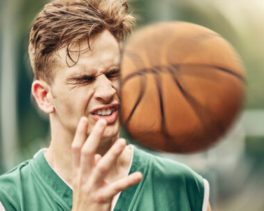 Sports, basketball and accident with face in game match on athlete court for tournament training. Injured man in professional outdoor fitness centre in pain from impact of ball hit action.