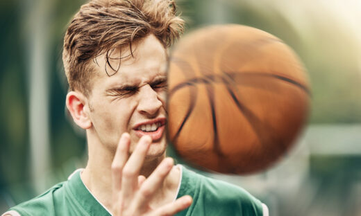Sports, basketball and accident with face in game match on athlete court for tournament training. Injured man in professional outdoor fitness centre in pain from impact of ball hit action.