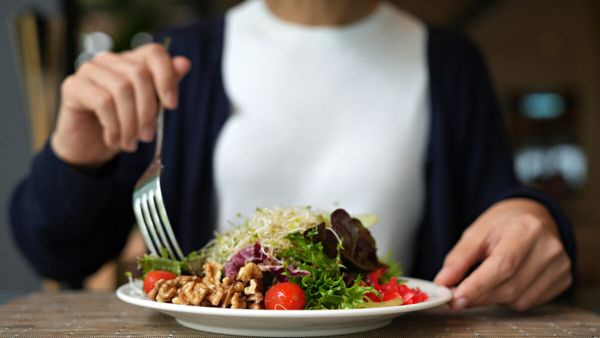 Vibrant arrangement of green salad consisting of alfalfa sprouts, cherry tomatoes, walnuts, leafy vegetables, olives, and drizzled with salad dressing. This dish represents a delicious and nutritious option for those following a vegan diet.