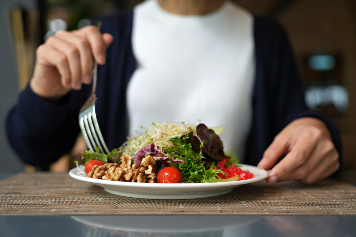Vibrant arrangement of green salad consisting of alfalfa sprouts, cherry tomatoes, walnuts, leafy vegetables, olives, and drizzled with salad dressing. This dish represents a delicious and nutritious option for those following a vegan diet.