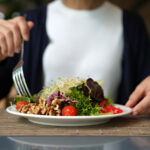 Vibrant arrangement of green salad consisting of alfalfa sprouts, cherry tomatoes, walnuts, leafy vegetables, olives, and drizzled with salad dressing. This dish represents a delicious and nutritious option for those following a vegan diet.