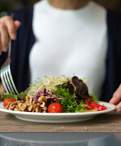 Vibrant arrangement of green salad consisting of alfalfa sprouts, cherry tomatoes, walnuts, leafy vegetables, olives, and drizzled with salad dressing. This dish represents a delicious and nutritious option for those following a vegan diet.