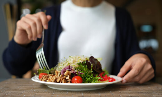 Vibrant arrangement of green salad consisting of alfalfa sprouts, cherry tomatoes, walnuts, leafy vegetables, olives, and drizzled with salad dressing. This dish represents a delicious and nutritious option for those following a vegan diet.