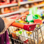 Close up of a woman's hand on a supermarket trolley, filling up with products during a weekly shop.