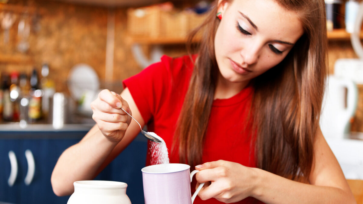 "girl putting white sugar in her tea or coffee - unhealthy lifestyle :)focus on coffee cup & spoon with sugar, the girl & the kitchen is defocused"