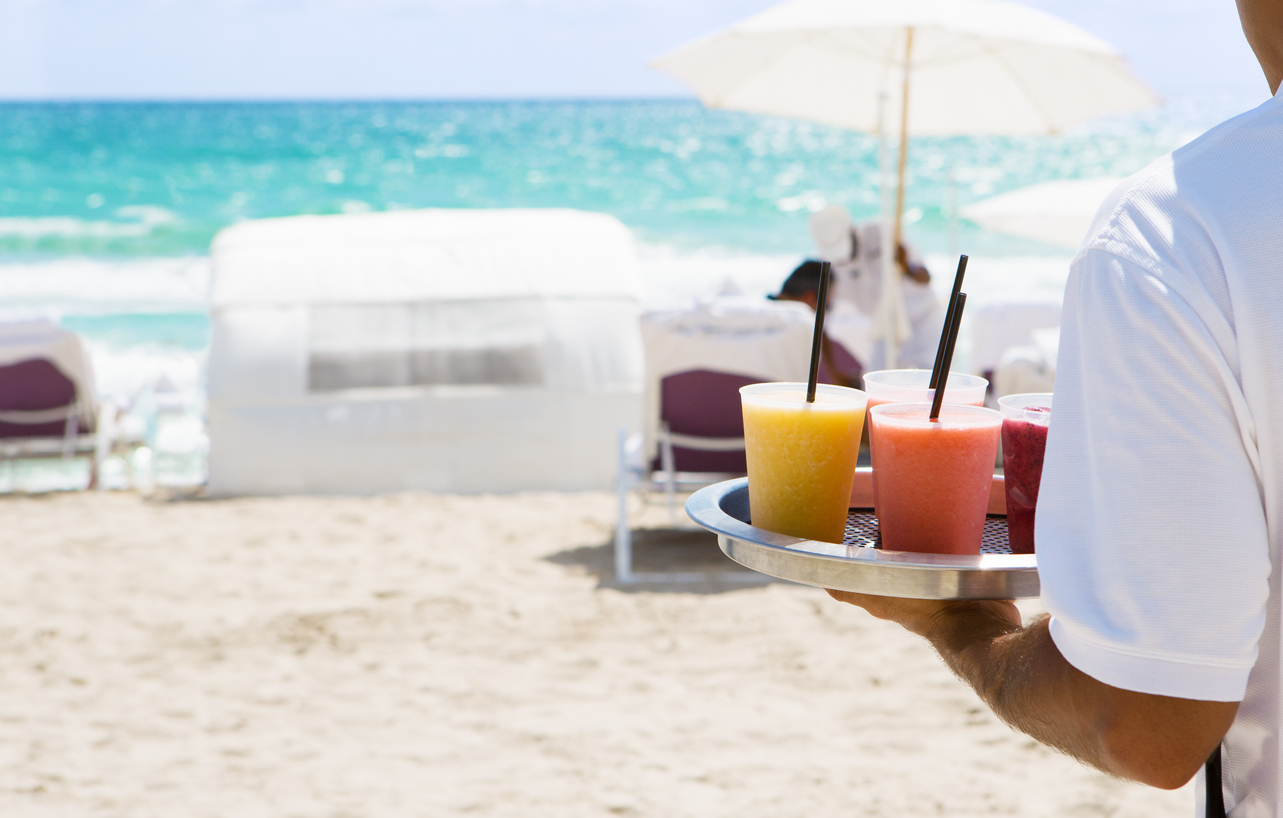 Waiter brings cocktail to resort guests on the beach