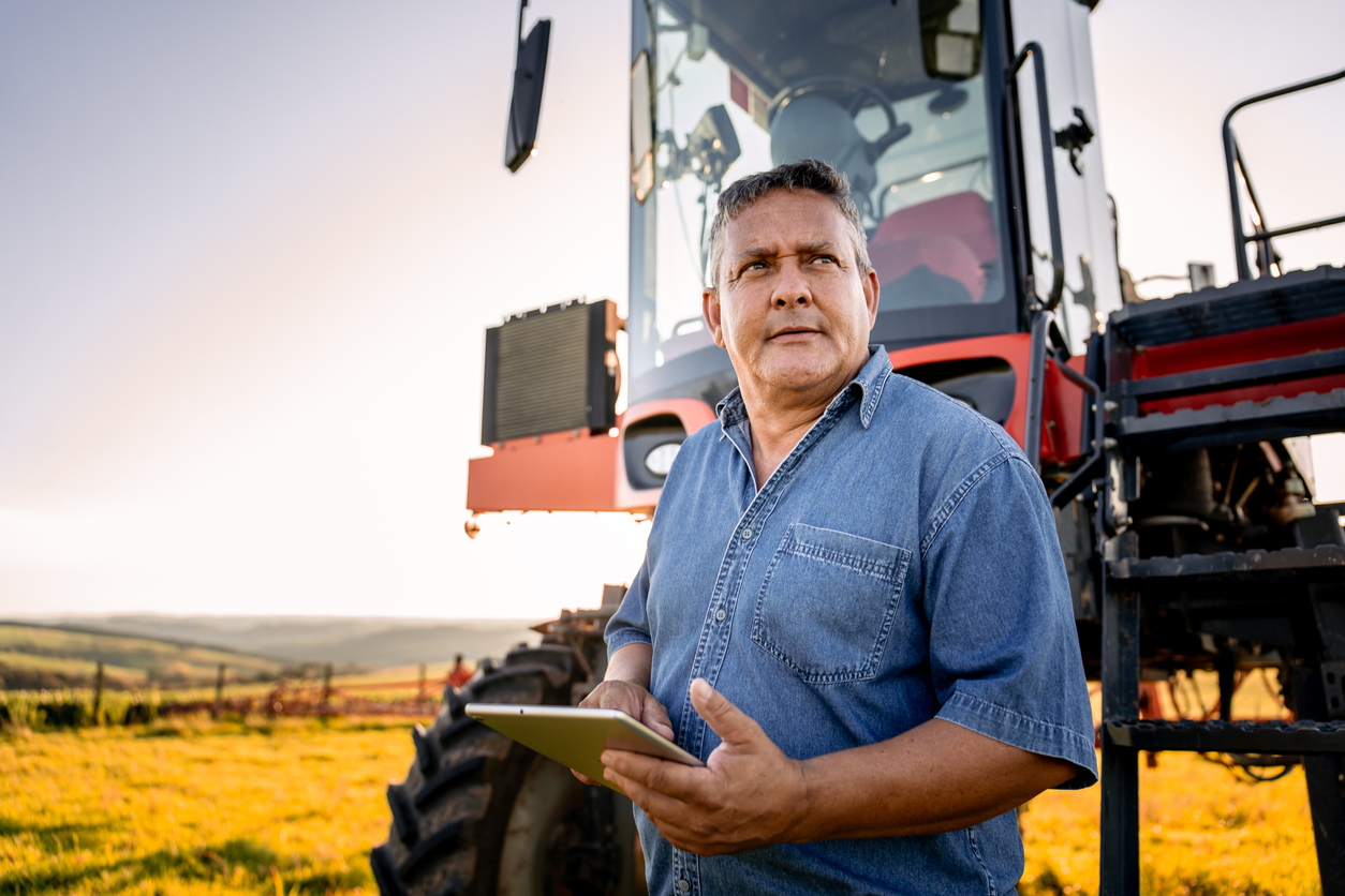 Portrait of an agronomist with a tablet in front of the agricultural machine