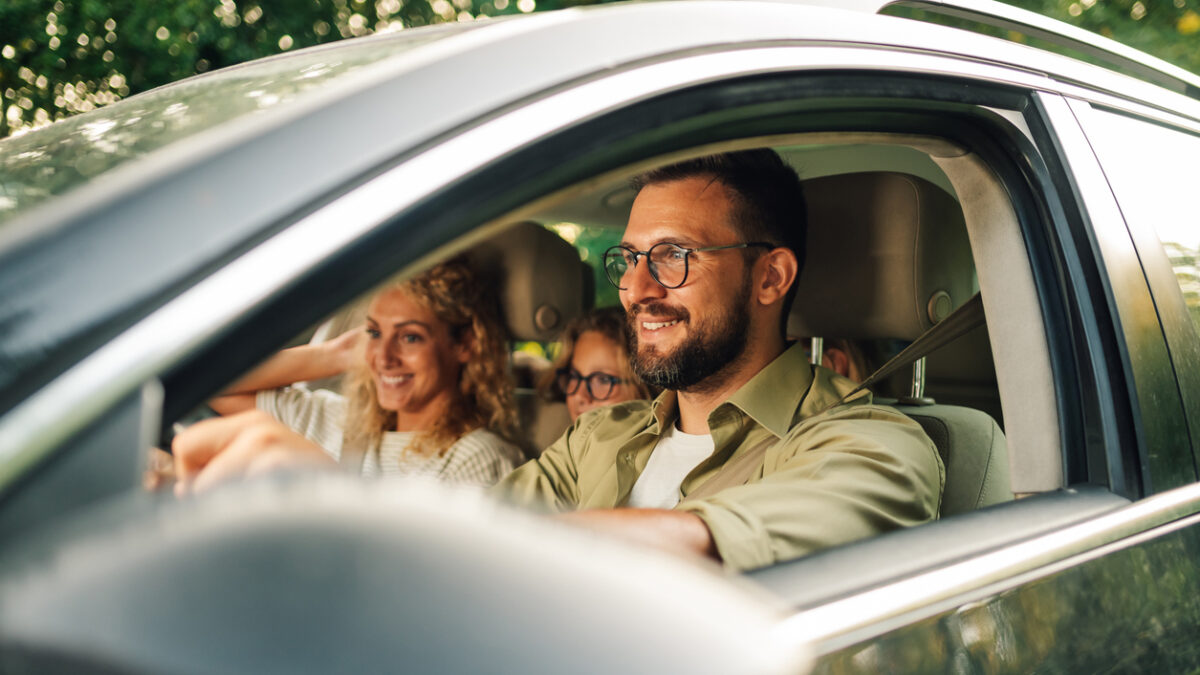 Portrait of a father driving a new car or having a test drive in the city while riding with his family. Parents and daughters spending vacation traveling by automobile and enjoying road trip.