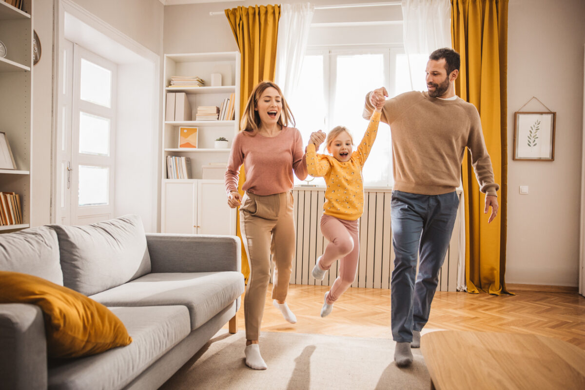 Happy family, mother, father and daughter jumping and playing at home.