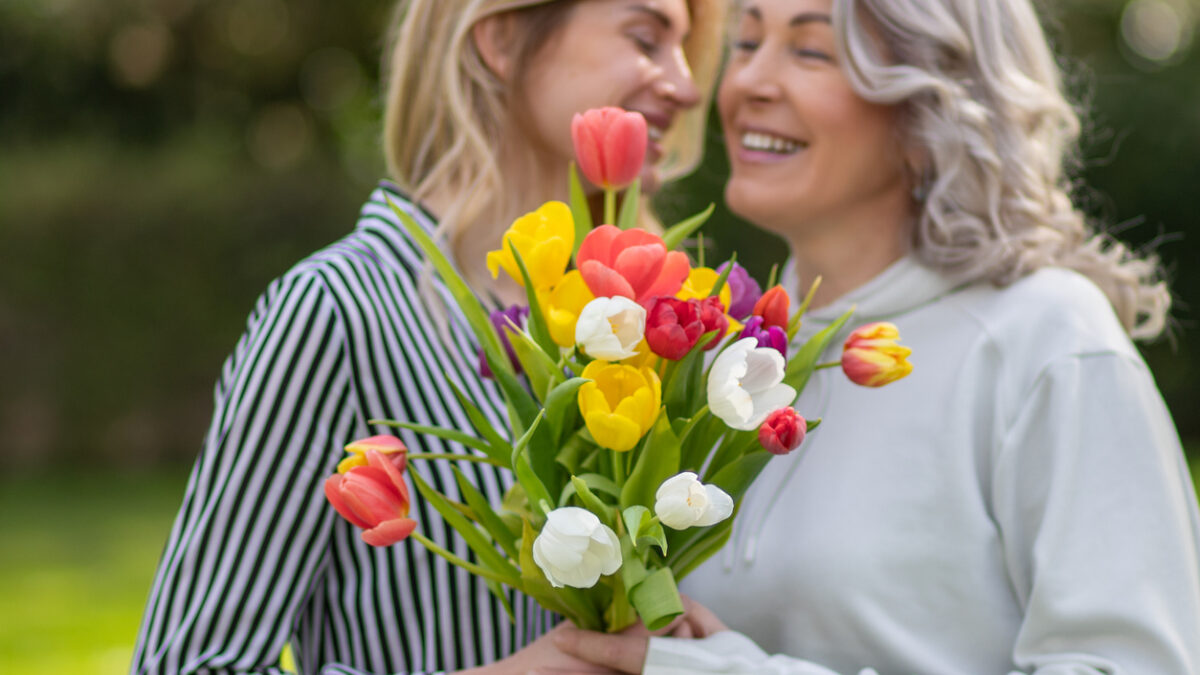 Daughter hugs mother, focus on tulip bouquet.