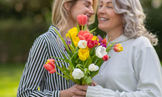 Daughter hugs mother, focus on tulip bouquet.