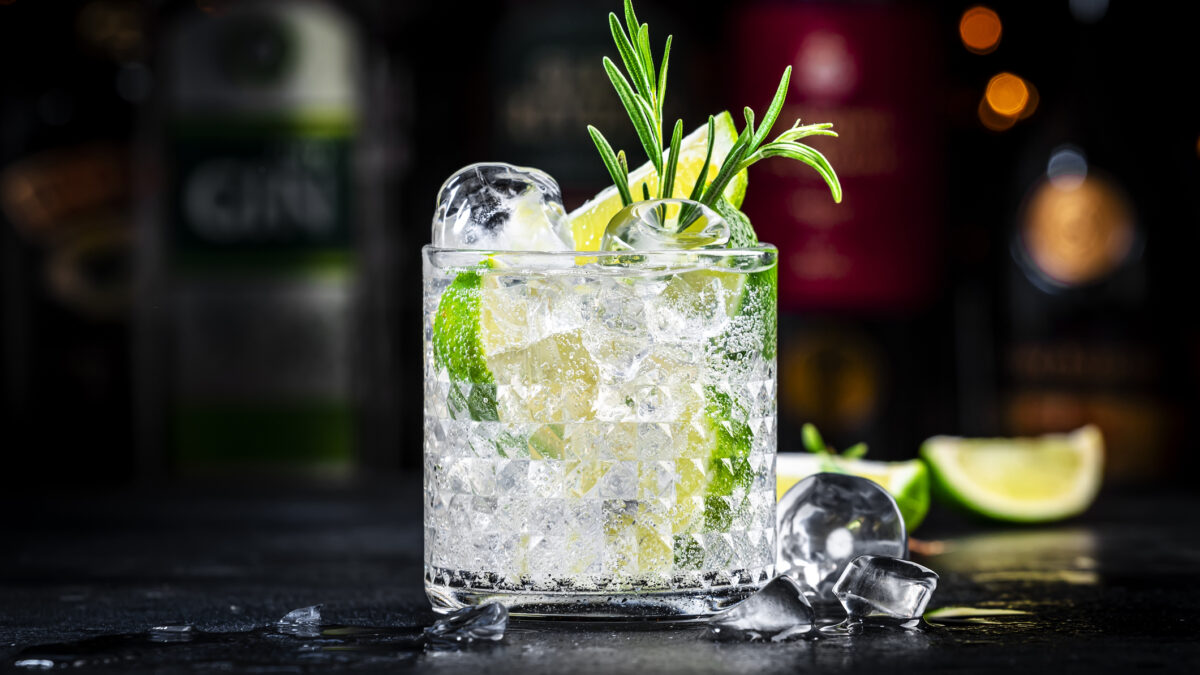 Gin tonic and rosemary cocktail drink with lime juice, sugar syrup, soda and ice. Black bar counter background