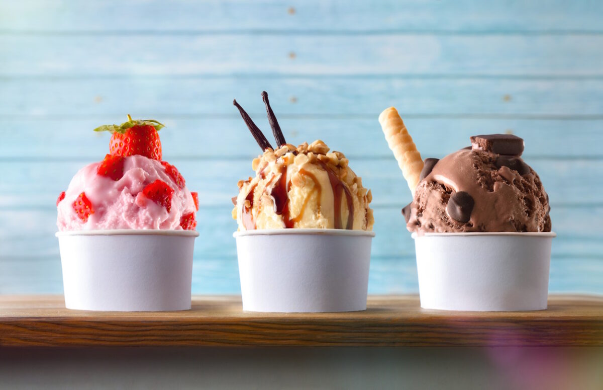 Three glasses of ice cream with strawberry, vanilla and chocolate balls decorated on a wooden table and blue slatted background. Front view.