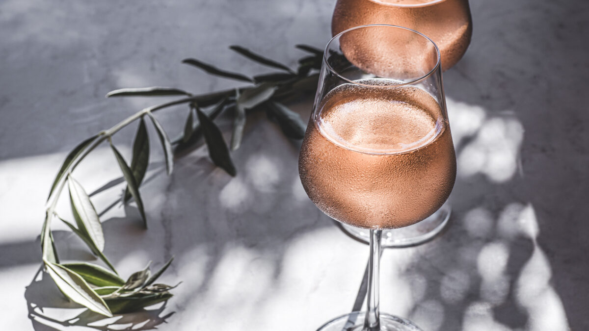 Rose wine in glasses on a table in the sun's rays, olive branches. Mediterranean, California wine, winery, summer vibes