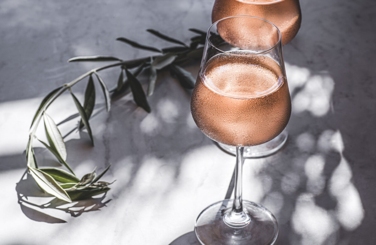 Rose wine in glasses on a table in the sun's rays, olive branches. Mediterranean, California wine, winery, summer vibes