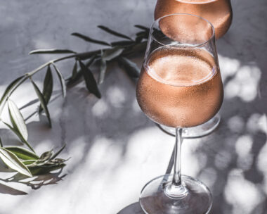 Rose wine in glasses on a table in the sun's rays, olive branches. Mediterranean, California wine, winery, summer vibes