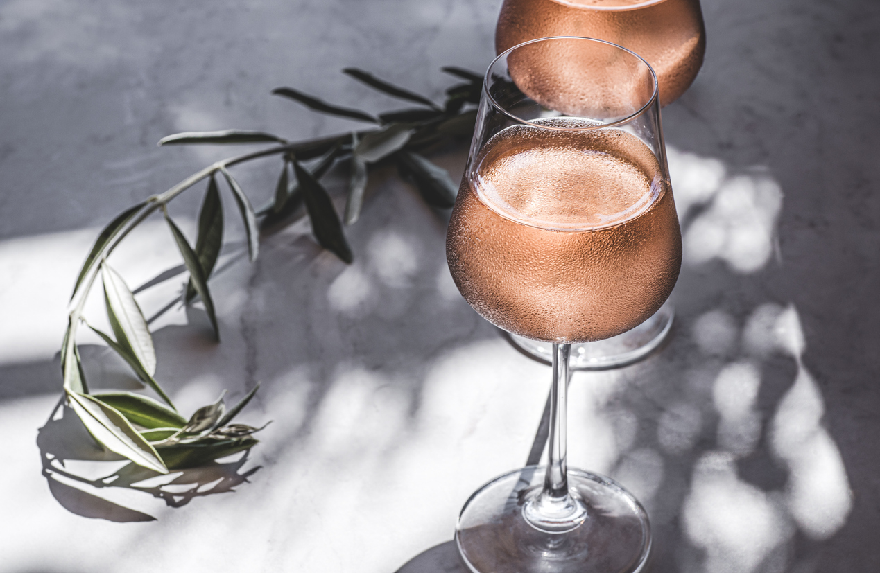 Rose wine in glasses on a table in the sun's rays, olive branches. Mediterranean, California wine, winery, summer vibes